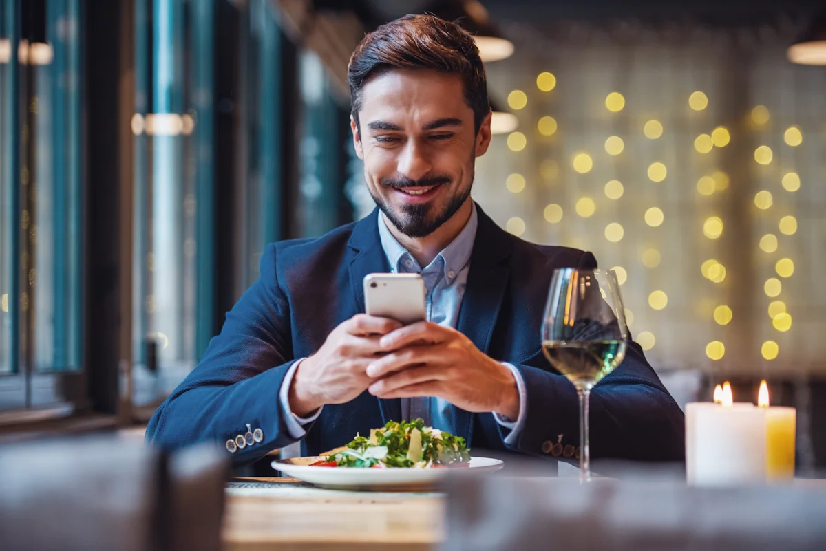 Un homme qui scrolle sur son smartphone pendant un dinner en amoureux