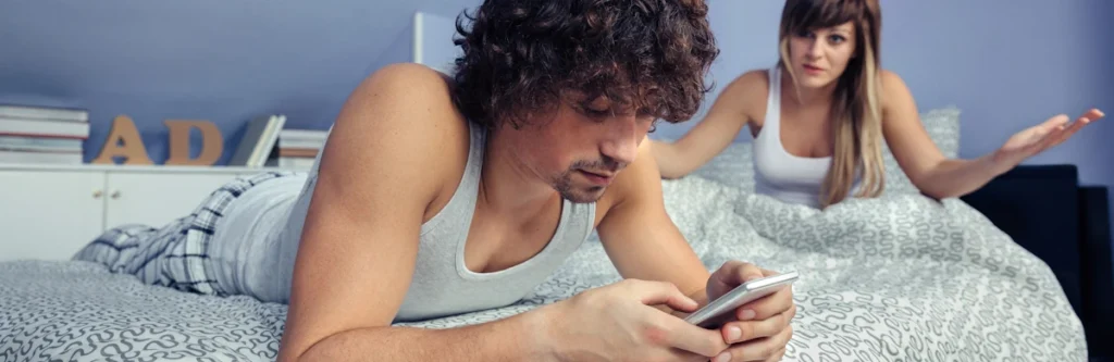 Un homme sur son téléphone devant son femme dans le lit